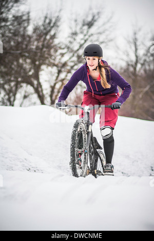 Mitte Erwachsenen weiblichen Mountainbiker kämpfen durch Schnee zu reiten Stockfoto