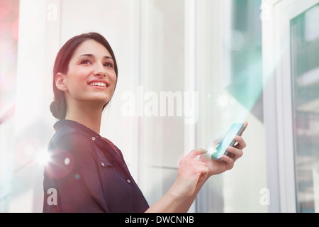 Junge Geschäftsfrau hält Smartphone mit Lichtern, die daraus Stockfoto