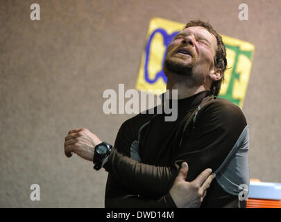 Anchoarge, AK, USA. 4. März 2014. BOB HALLINEN / Anchorage Daily News.Musher Jason Mackey zuckt vor Schmerz, als er seinen Arm bewegt sich in der Cafeteria der Schule am Checkpoint Nikolai während des Iditarod Trail Sled Dog Race auf Dienstag, 4. März 2014. © Bob Hallinen/Anchorage Daily News/ZUMAPRESS.com/Alamy Live News Stockfoto