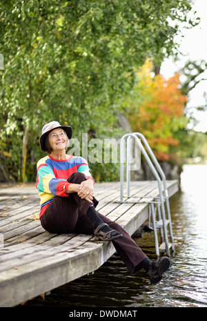 Nachdenklich senior Frau sitzt am pier Stockfoto