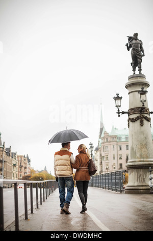 Rückansicht des jungen Paares mit Regenschirm zu Fuß auf die Brücke Stockfoto