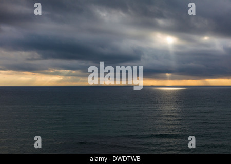 Sonnenstrahlen gleiten durch die Wolken über ein ruhiges Meer Stockfoto