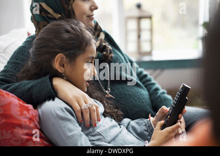 Tochter mit Fernbedienung sitzend mit Mutter zu Hause Stockfoto