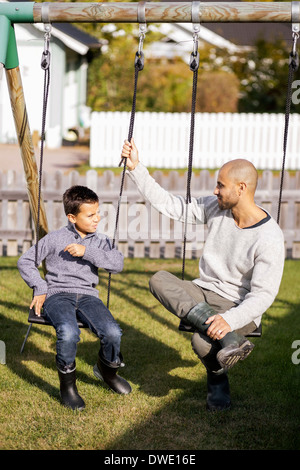 Vater und Sohn sitzen auf der Schaukel im Garten Stockfoto