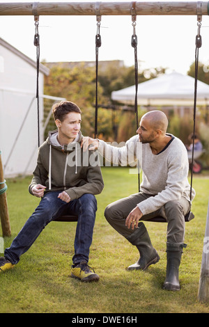 Vater und Sohn sitzen auf der Schaukel im Garten Stockfoto