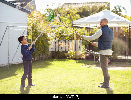 Vater und Sohn kämpfen mit Rechen im Garten Stockfoto