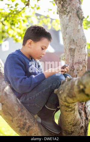 Seitenansicht eines jungen mit Handy auf Baum sitzend Stockfoto