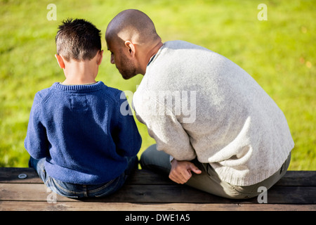 Rückansicht von Vater und Sohn sitzen am Hof Stockfoto