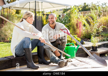 Volle Länge des reifes Paar mit Gartengeräten sitzt am Hof Stockfoto