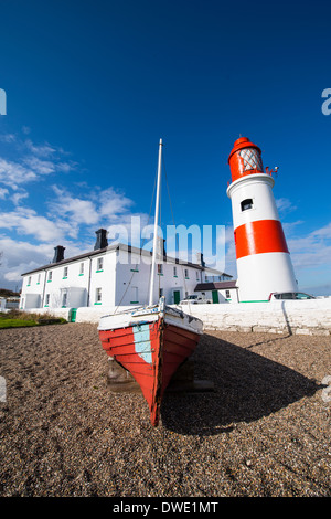 Ein rotes Boot sitzt im Vordergrund eines Bildes von der rot-weißen Leuchtturm und weißen Hüter-Hütte am Souter Punkt. Stockfoto