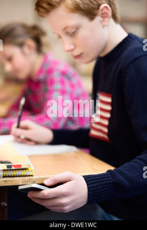 Gymnasiast mit Smartphone während des Studiums im Klassenzimmer Stockfoto
