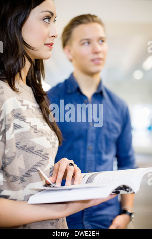 Junge Studentin, Buch mit Freund im Hintergrund hält. Stockfoto