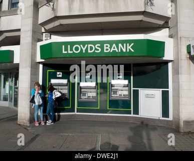 Zwei Mädchen im Teenageralter SMS auf dem Handy außerhalb Lloyds Bank Geldautomaten in Cardiff City Centre Wales UK KATHY DEWITT Stockfoto