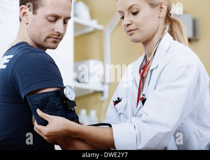 Ärztin Verpackung Manschette um den Arm des Patienten vor der Einnahme von Blutdruck in Klinik Stockfoto