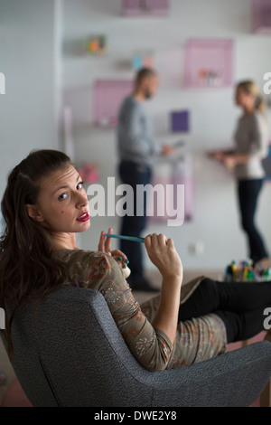 Porträt der Geschäftsfrau sitzend auf Stuhl während Kollegen stehen im Hintergrund im Büro Stockfoto