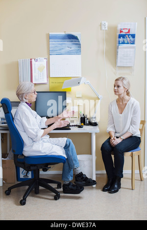 Gesamte Länge der leitende Ärztin im Gespräch mit Frau in Klinik Stockfoto