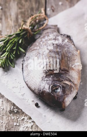 Dorado Rohfisch mit Rosmarin und Meer Salz Server auf weißem Papier über alten Holztisch. Serien ansehen Stockfoto