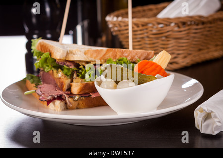 Köstliche dünn geschnittenes Rindfleisch Pastrami Clubsandwich mit frischem lockige Salat serviert mit einer kleinen Schüssel mit eingelegtem Gemüse auf einem weißen Teller, isoliert auf weiss Stockfoto