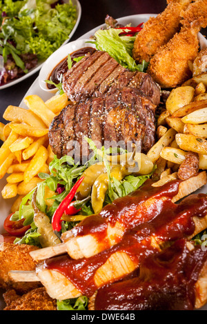 Gesunde Platte mit gemischtem Fleisch einschließlich gegrilltes Steak, knusprig Panierter Hühner- und Rindfleisch auf einem Bett aus frischen grünen grün gemischter Salat serviert mit Pommes Frites und Chutney oder BBQ-Sauce in eine Schüssel Stockfoto