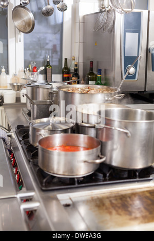 Kochen in einer Großküche mit großen Edelstahl-Töpfe gefüllt mit Eintopf und Gemüse auf einem zentralen Gaskochfeld Stockfoto