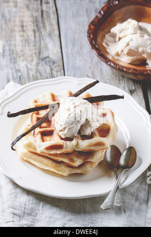 Frische Waffeln und Schüssel mit Eis, serviert mit Vanille-Sticks über Holztisch. Stockfoto