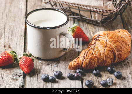 Frische Croissant mit Vintage Tasse Milch und Beeren über alten Holztisch. Stockfoto