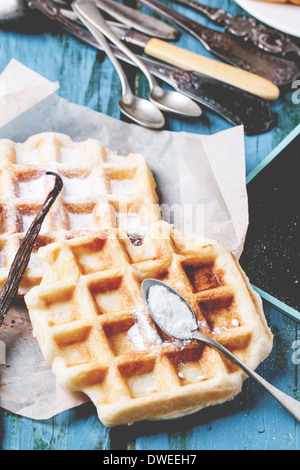 Frische Waffeln mit Puderzucker und Vintage Besteck über blaue Holztisch serviert. Stockfoto