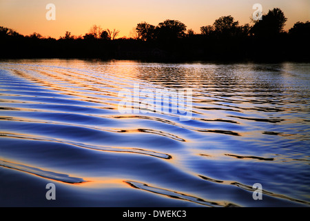 Wellen im Zuge von einem Ponton-Boot bei Sonnenuntergang auf Whitewood See, Teil der Huron River-Kette von Seen, Michigan, USA Stockfoto