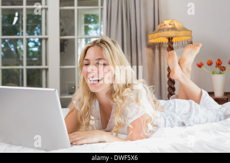 Fröhliche lässige Frau mit Laptop im Bett Stockfoto