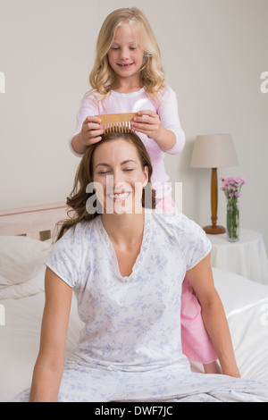 Niedliche Mädchen Kämmen glückliche Mutter Haare im Schlafzimmer Stockfoto