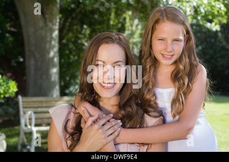 Mädchen umarmt ihre Mutter von hinten im park Stockfoto