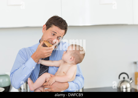 Beschäftigt Vater hält seinen Sohn vor der Arbeit und Toast Essen Stockfoto