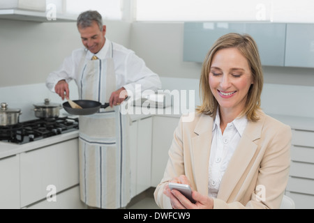Geschäftsfrau von SMS-Nachrichten während Mann, die Zubereitung von Speisen in der Küche Stockfoto