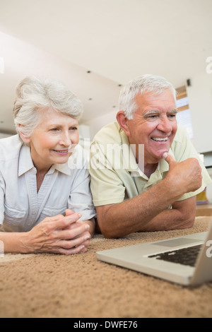 Fröhliche älteres Paar mit dem Laptop zusammen liegend auf Teppich Stockfoto