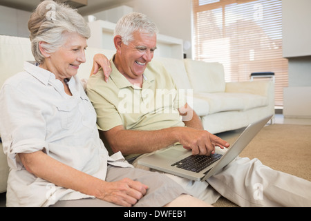 Fröhliche älteres Paar mit Laptop zusammen sitzen auf Teppich Stockfoto
