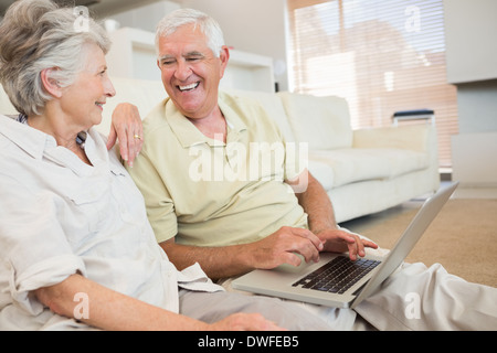Fröhliche älteres Paar mit Laptop zusammen sitzen auf Teppich Stockfoto