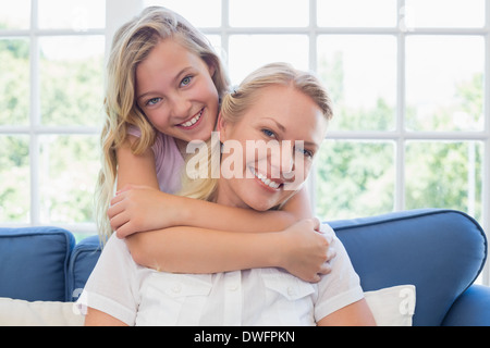 Mädchen, die Mutter von hinten in Wohnzimmer umarmen Stockfoto