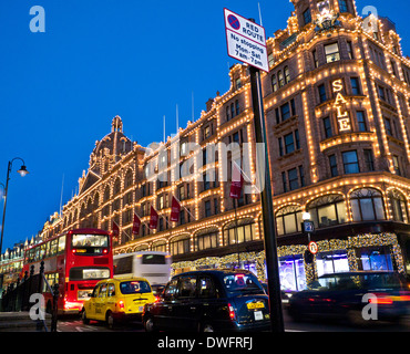 Harrods verkauf Beleuchtung Dämmerung Kaufhaus mit beleuchteten Ale' Zeichen Käufer rote Route Zeichen Bus und Taxis auf rote Route Knightsbridge London SW1 Stockfoto