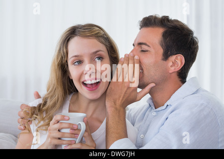 Mann Geheimnis in einer fröhlichen jungen Womans Ohr flüstern Stockfoto