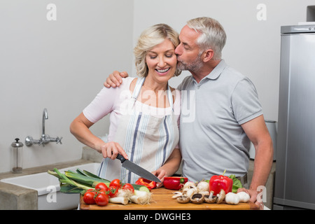 Mann, die Frau zu küssen, wie sie Gemüse in der Küche hackt Stockfoto