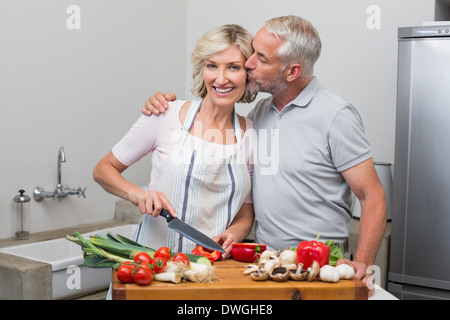 Mann, die Frau zu küssen, wie sie Gemüse in der Küche hackt Stockfoto