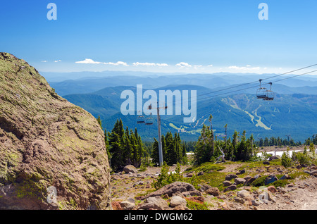 Sessellift hinauf Mount Hood mit Wald bedeckt, Hügel im Hintergrund und einem großen Felsbrocken im Vordergrund Stockfoto