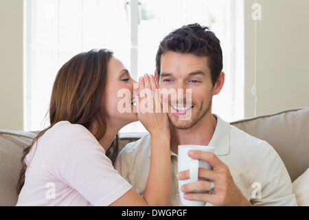 Flüstern Geheimnis in eine glückliche Frau mans Ohr im Wohnzimmer Stockfoto