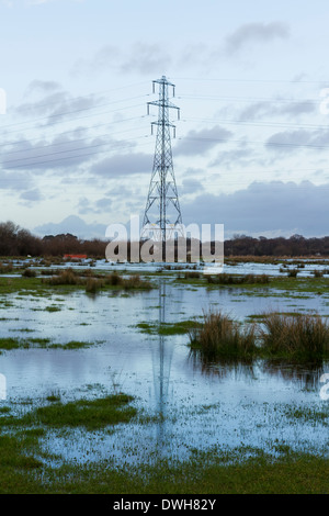 Hochspannung Pylon mit seinen Überlegungen in überschwemmten Wiesen Christchurch, Dorset, England, Vereinigtes Königreich. Stockfoto