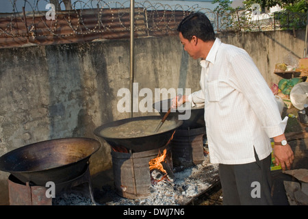 Ein Koch ist Suppe mit einer Kelle rühren, wie er traditionelle Khmer-Suppe in großer Wok auf einer Stadtstraße in Kampong Cham, Kambodscha kocht Stockfoto