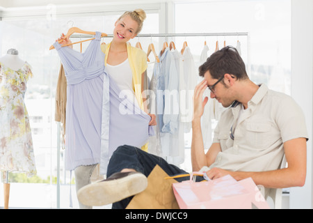 Gelangweilt Mann mit Einkaufstaschen während Frau am Kleiderständer Stockfoto