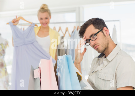 Gelangweilt Mann mit Einkaufstaschen während Frau am Kleiderständer Stockfoto