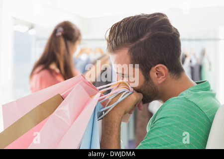 Gelangweilt Mann mit Einkaufstaschen während Frau von Kleiderständer Stockfoto