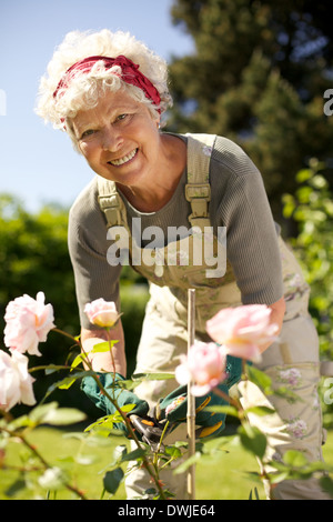 Porträt von schöne ältere Frau kümmert sich um die Pflanzen in ihrem Garten betrachten Sie lächelnd - Seniorin im Garten im Hinterhof Stockfoto