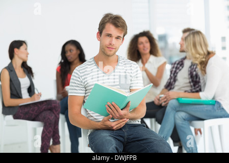 Glücklicher Mann Notebook zu halten, während die Kollegen hinter ihm sprechen Stockfoto